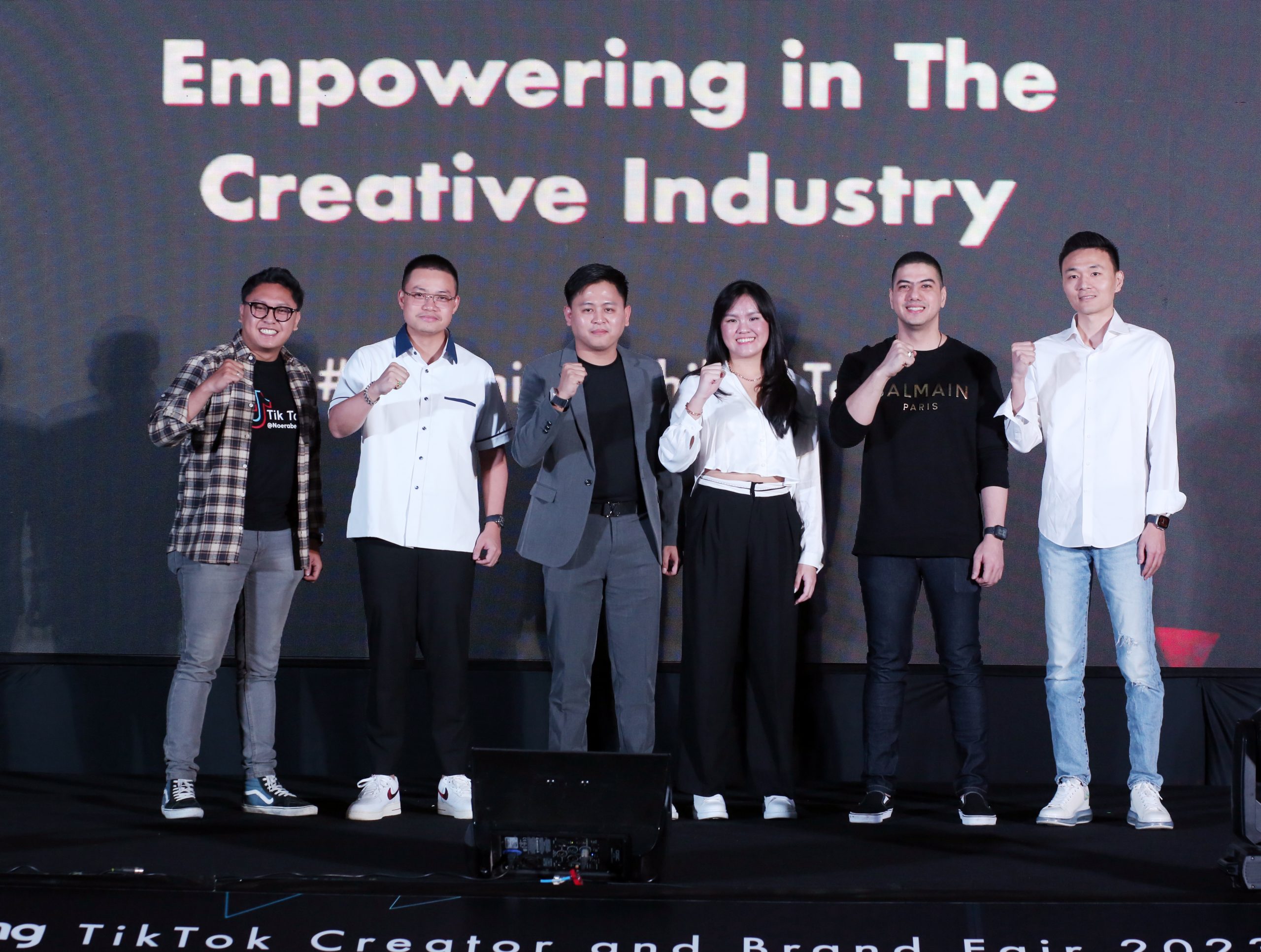  A group of six people standing on a stage with the text "Empowering in the Creative Industry" behind them.